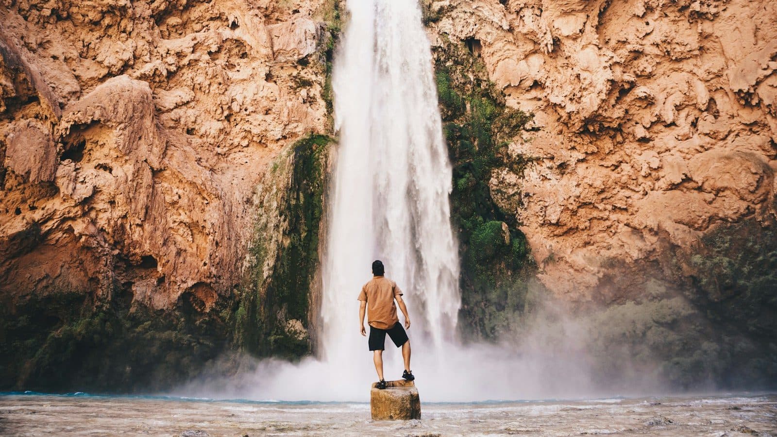 man standing on stone in front of waterfall